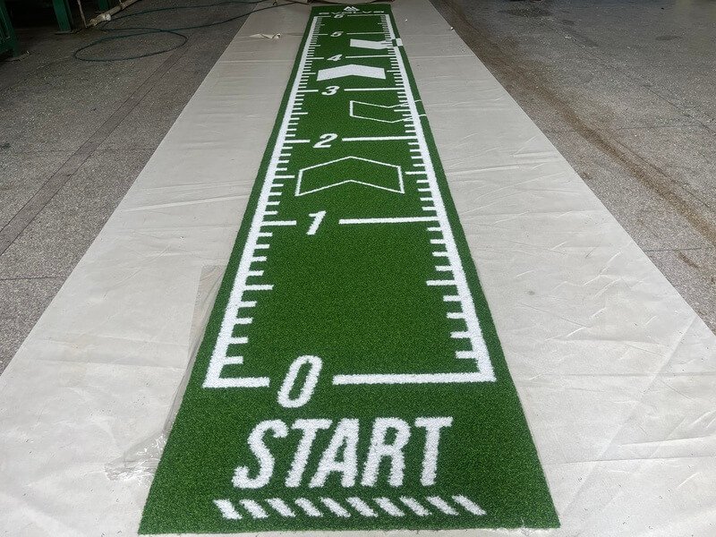Athlete performing battle ropes on a green padded turf lane in a spacious gym